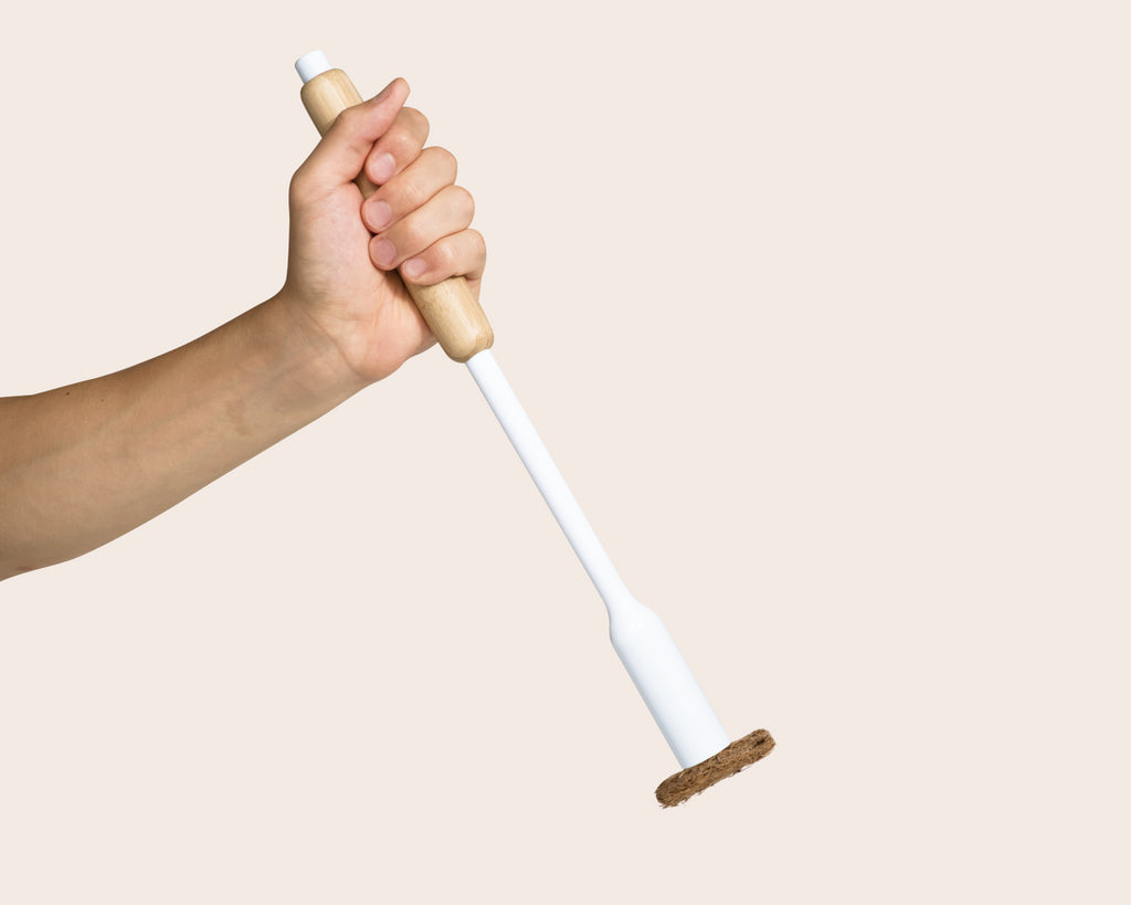 Hand holding a white toilet brush with bamboo handle against a beige background