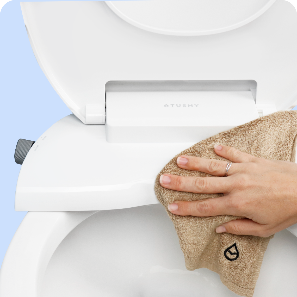 Hand wiping down the Tushy WAVE bidet toilet seat with a soft, beige towel with the Tushy droplet logo embroidered in dark brown