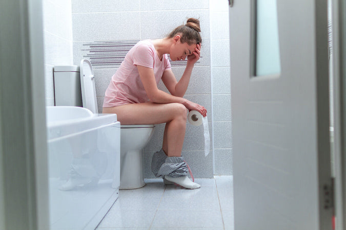 Despondent looking woman on the toilet, holds her head in her hand