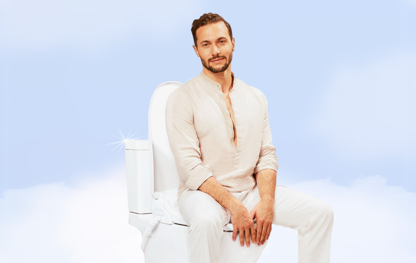 A man sitting on a toilet in a linen shirt gazing at the camera.