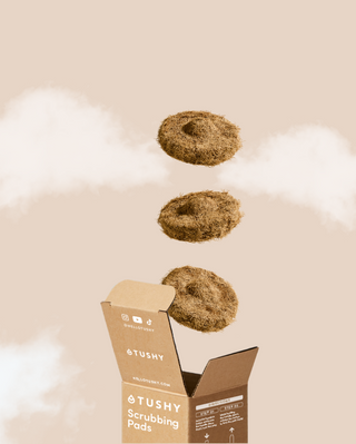TUSHY scrubbing pads on a beige background with an open cardboard box.