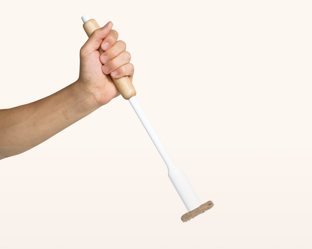 Hand holding a white Tushy Toilet Brush with bamboo handle on a white background