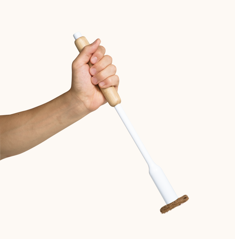 Hand holding a white toilet brush with a bamboo handle and coconut husk scrubbing pad on a white background