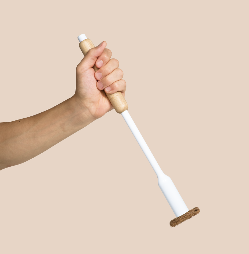Hand holding a white toilet brush with a bamboo handle against a beige background