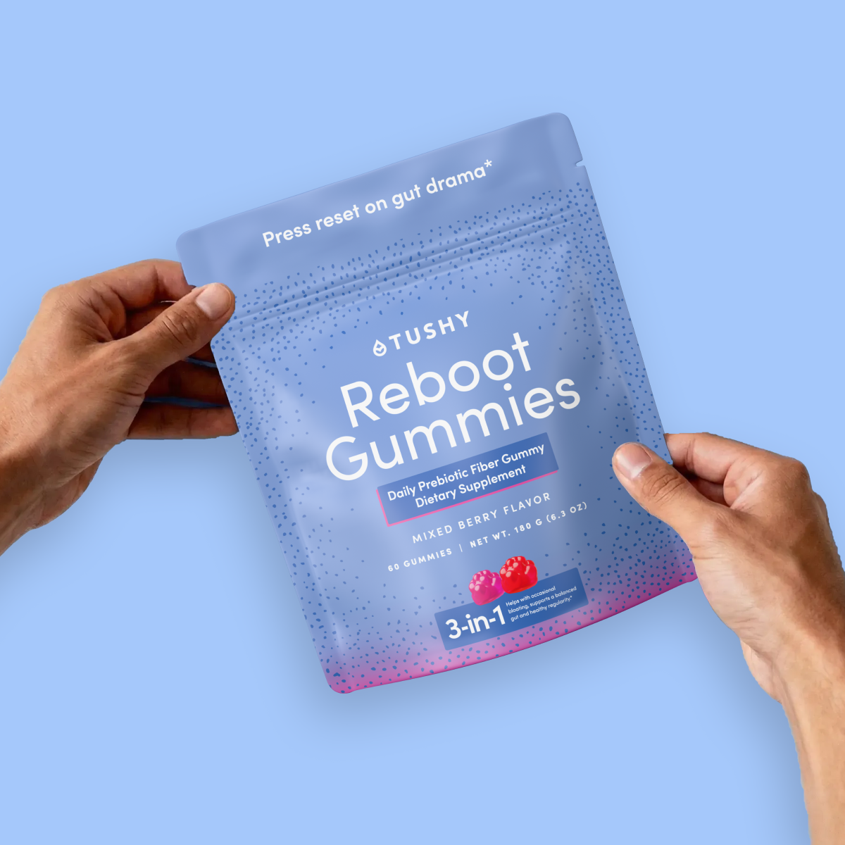 Hands holding a package of Tushy Reboot Gummies against a light blue background