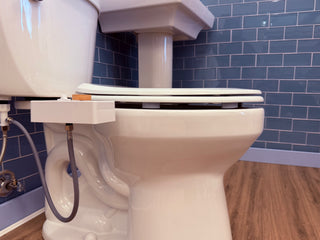 Toilet with a white seat and bumpers, positioned next to a wall with blue tiles and a wooden floor.