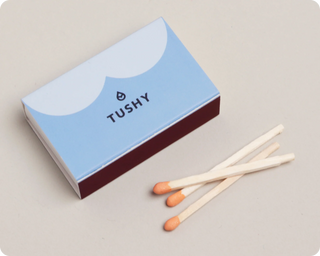 A matchbox with a blue and white design featuring the word "TUSHY" and three wooden matches with orange tips.