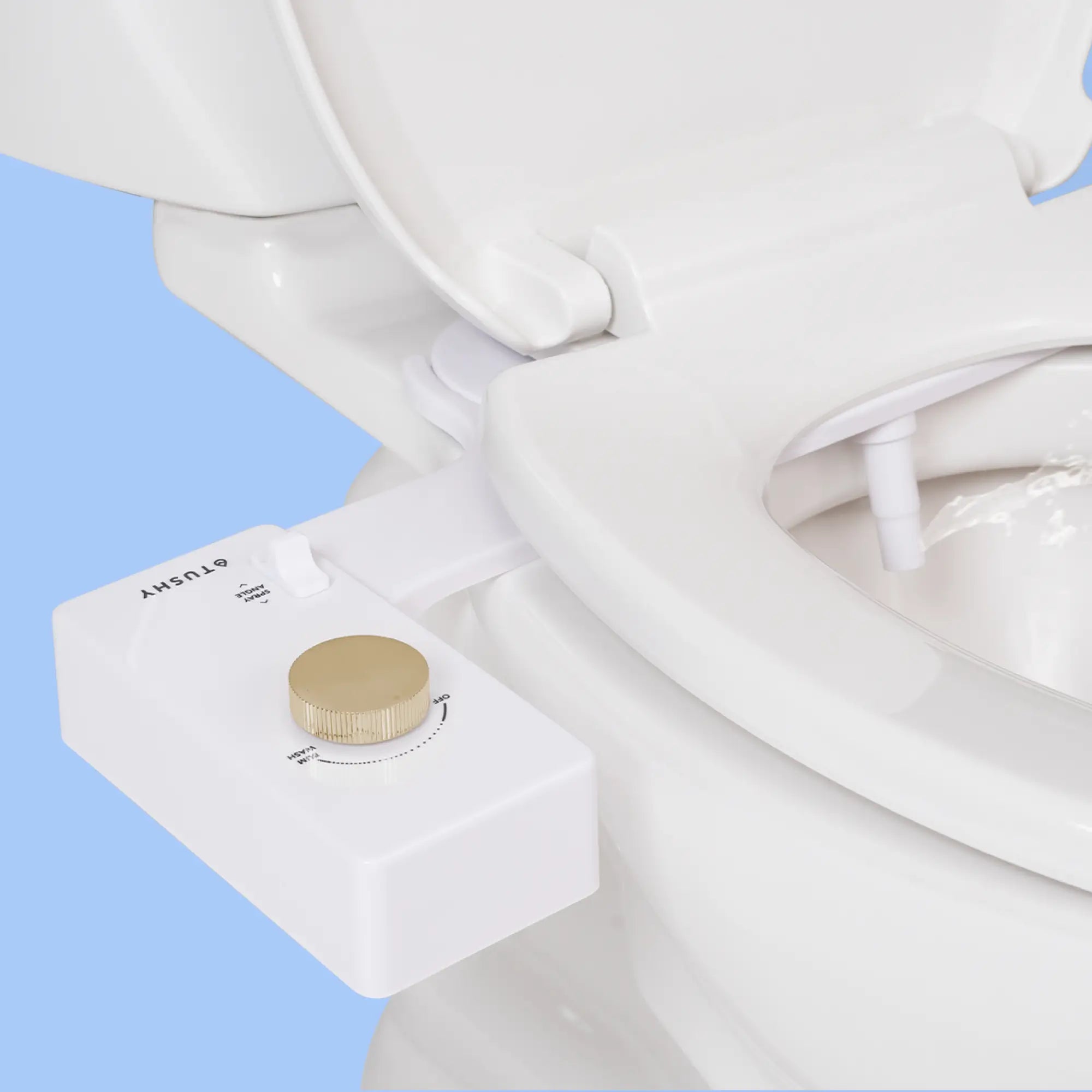 White 'TUSHY' Classic console, with a gold pressure control knob, installed on a toilet, on a light blue background