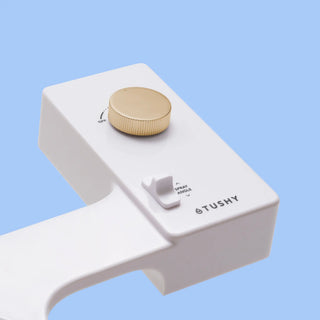 White 'TUSHY' Classic console, with a gold pressure control knob, on a light blue background