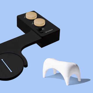 Black TUSHY Spa console with 2 gold knobs, and a white Tushy ottoman, on a blue background