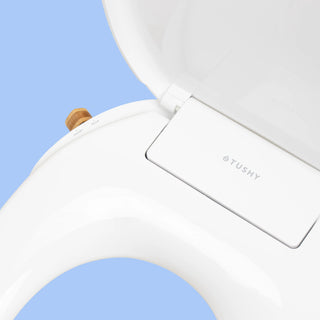 White TUSHY Wave bidet seat closeup, with a bamboo knob, on a blue background