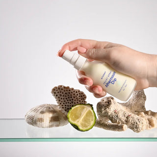 Hand holding a bottle labeled 'Afternoon Dip' with natural elements like lime and coral in the background.