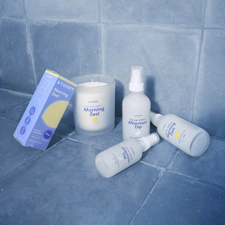 Collection of Tushy products including bottles and a candle on a tiled floor.