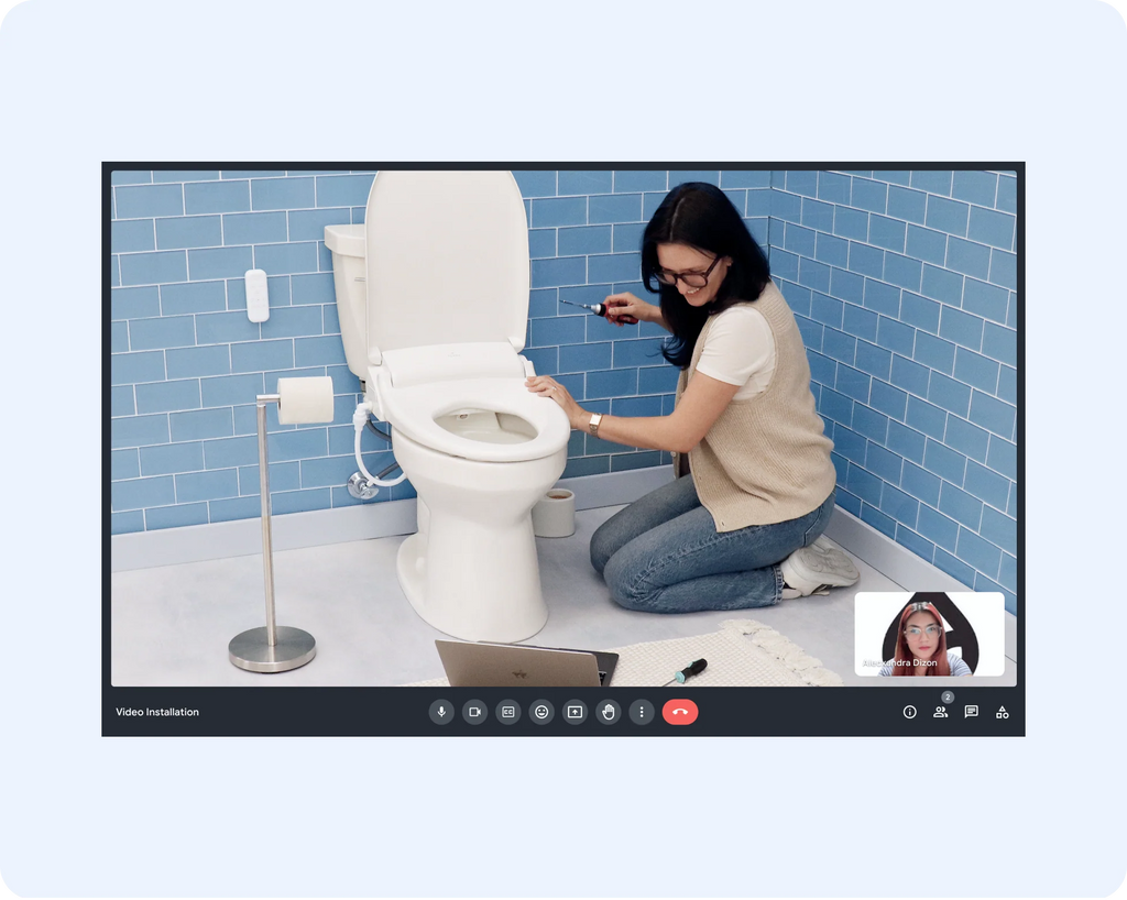 Screencapture of a woman kneeling next tot he toilet in her bathroom, on a video call with a Tushy expert, getting help with installation