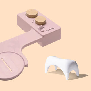 Pink bidet attachment with wooden knobs and a white footstool, designed for bathroom use.