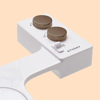 White bidet attachment with two metal knobs for water temperature and spray angle adjustment.