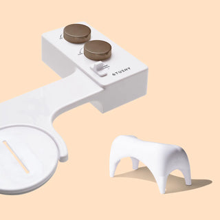 White bidet attachment with two control knobs and a small stool for improved positioning.