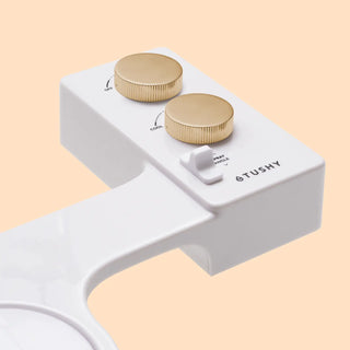 White bidet attachment with two gold knobs for temperature and spray angle adjustment.
