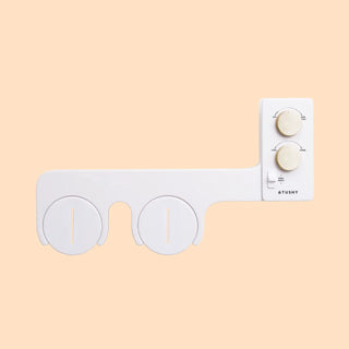White bidet attachment with two circular nozzles and control knobs for water temperature and pressure.