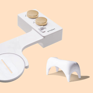 White bidet attachment with gold knobs for water pressure and temperature control, alongside a small white stool.