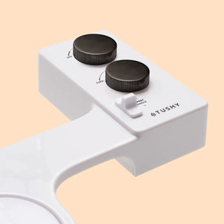 White bidet attachment with two black knobs for water temperature and spray angle adjustment.