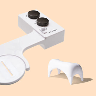White bidet attachment with two control knobs and a small stool for improved positioning.