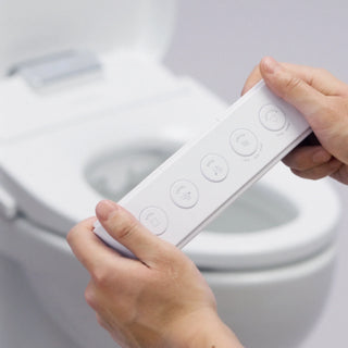 A person holds a white remote control with buttons in front of a toilet.